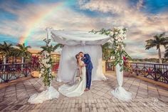 a bride and groom kissing under an arch with a rainbow in the background