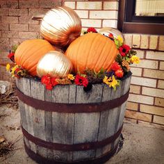 pumpkins and gourds are sitting in a barrel on the ground next to a brick wall