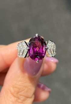 a woman's hand holding a ring with a purple stone and diamonds on it