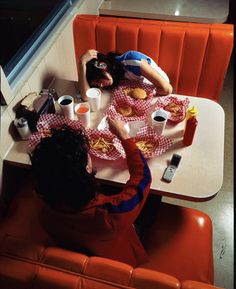 two people sitting at a table with food and drinks in front of them on red chairs