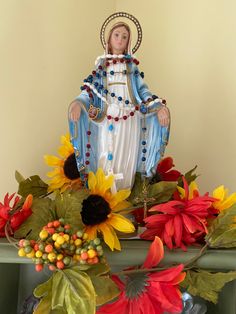 a statue of the virgin mary surrounded by autumn leaves and sunflowers on a mantle