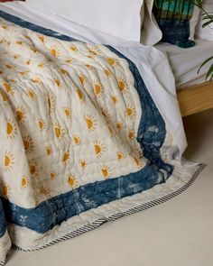 an unmade bed with white and blue bedspread next to a potted plant