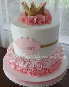 a white cake with pink ruffles and a gold crown on top is sitting in front of a window