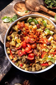 a large bowl filled with pasta salad next to wooden spoons and utensils