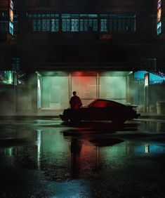 a man sitting on top of a car in front of a tall building at night