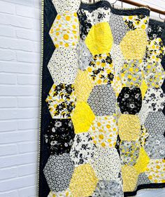 a black and yellow quilt hanging up against a white brick wall in front of a window