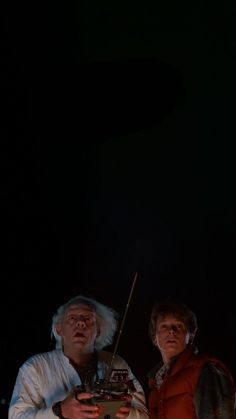 two men standing next to each other in front of a dark background with one holding a radio