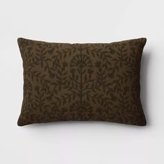 a brown and black pillow with leaves on it, against a white wall behind it