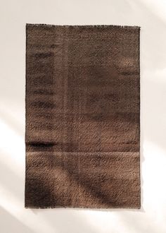 a brown area rug on a white wall with shadow from the light coming through it