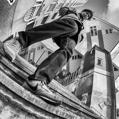 black and white photograph of skateboarder on the edge of a wall in front of a building