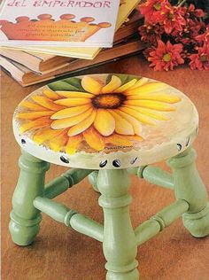 a green stool with a yellow flower painted on the seat and books in the background