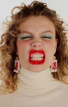 a woman with red lipstick and green eyes is making a funny face for the camera