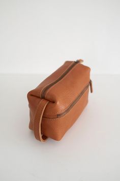 a tan leather toiletry bag on a white surface