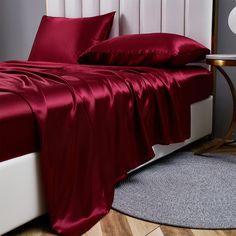 a bed with red sheets and pillows on top of it in a bedroom next to a night stand