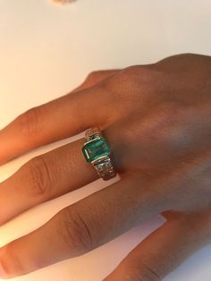 a woman's hand wearing a ring with an emerald colored stone on the middle