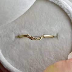 a gold ring with three leaves on it sitting in a white cloth box next to an apple