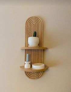 a wooden shelf with two bowls and a plant on it next to a white wall