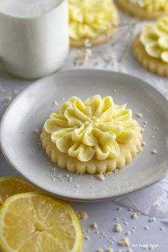 lemon cookies with icing and sprinkles sit on a plate next to a glass of milk