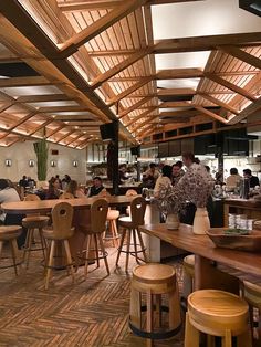 a restaurant with wooden tables and stools filled with people sitting at the bar area