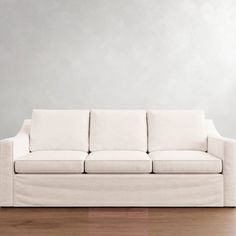 a white couch sitting on top of a hard wood floor next to a gray wall