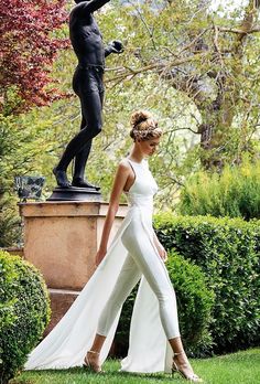 a woman is walking in front of a statue with her dress flowing down the side