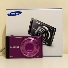 a purple samsung digital camera sitting next to a box