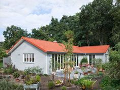 a white house with an orange roof surrounded by trees and plants in the foreground