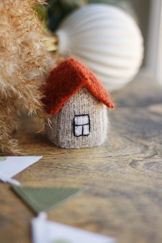 a knitted house sitting on top of a wooden table next to a teddy bear