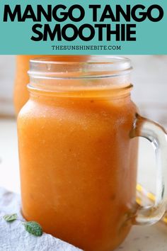 two mason jars filled with orange mango smoothie on top of a white cloth and green leaves