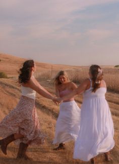 three women in white dresses are holding hands