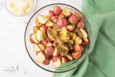 a glass bowl filled with potatoes and seasoning on top of a green cloth next to a white plate