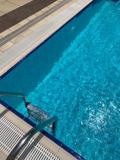 an empty swimming pool with blue water and tiled flooring on either side, next to a metal hand rail