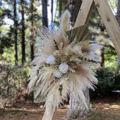 a wedding arch decorated with white flowers and pamolite feathers in the woods for an outdoor ceremony