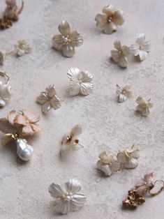 several pairs of flower shaped earrings laying on a white tablecloth with pearls and other beads