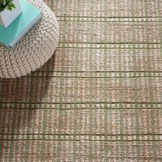 a green and white rug on the floor next to a table with a potted plant