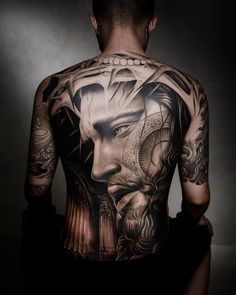 the back of a man's body with tattoos on his chest and head, in front of a dark background