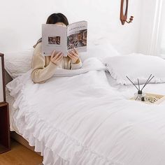 a woman is reading a book on her bed with white sheets and ruffled bedspread