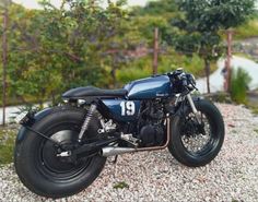 a blue motorcycle parked on top of a gravel covered ground next to trees and bushes