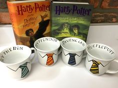 four harry potter mugs with ties on them and a book in the back ground