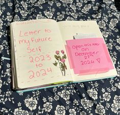 an open book with writing on it sitting on top of a flowery bed sheet