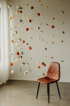 an orange chair sitting in front of a white wall with flowers hanging from the ceiling