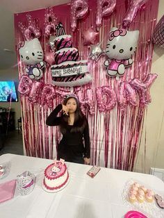 a woman standing in front of a table with pink balloons and hello kitty decorations on it