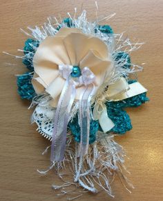 a brooch that is sitting on top of a wooden table with white and blue ribbons