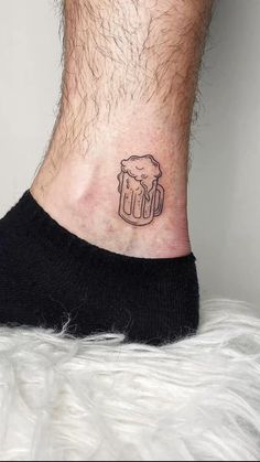 a man's foot with a small tattoo on the ankle that has a mug of beer