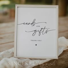 a card and gifts sign sitting on top of a wooden table next to a white cloth