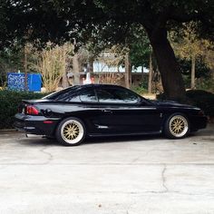 a black sports car parked in front of a tree and shrubbery with yellow rims