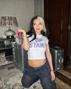 a woman in jeans and a crop top is posing for the camera while holding a water bottle