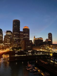 the city skyline is lit up at night, with boats in the water below it