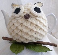 a knitted owl sitting on top of a white tea pot filled with green leaves