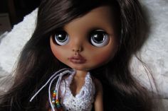 a close up of a doll with long brown hair wearing a white crochet dress